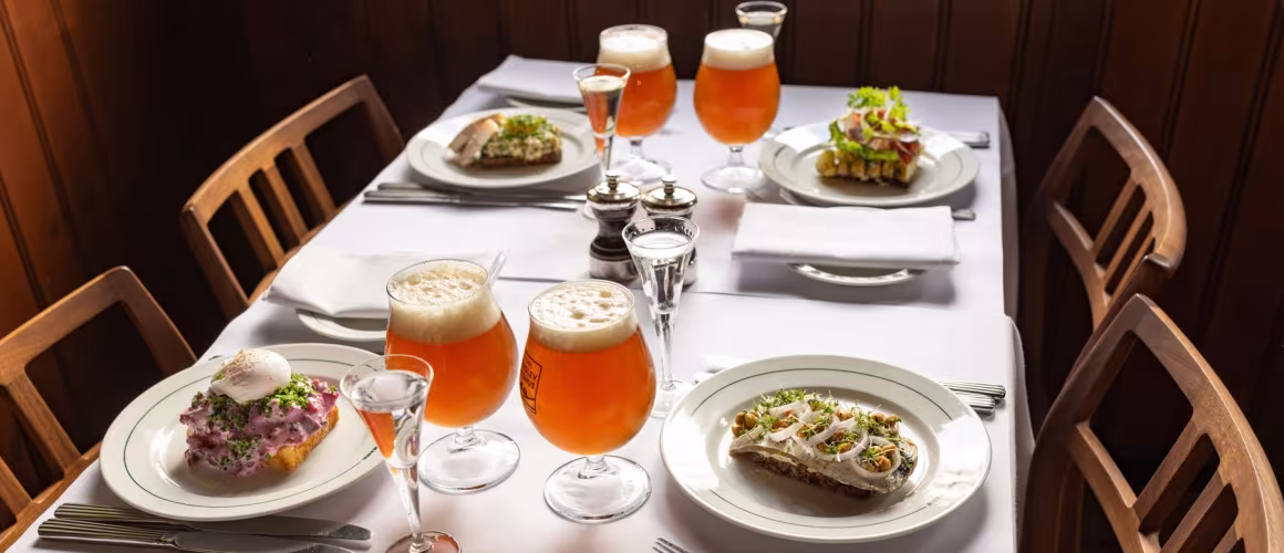 Dansk frokostbord med smørrebrød, øl og snaps i glas